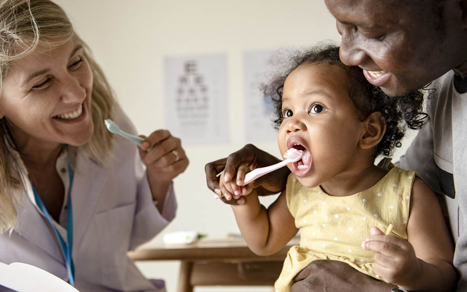 Image of physician helping parent and toddler learn to brush teeth